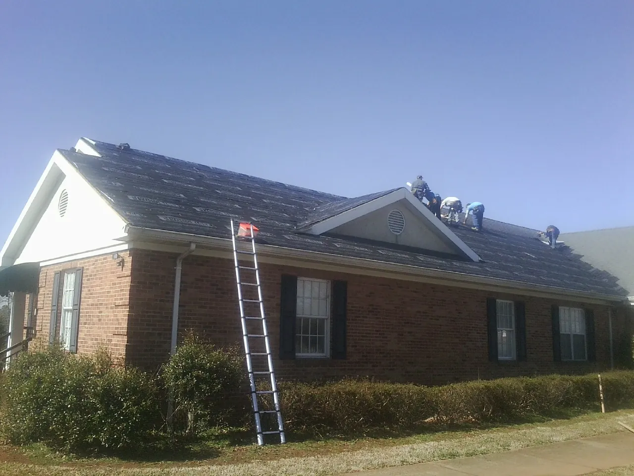Crew tearing shingles off a brick ranch roof with a ladder set — Emergency Roof Repair work by our crew in Mapleton Depot