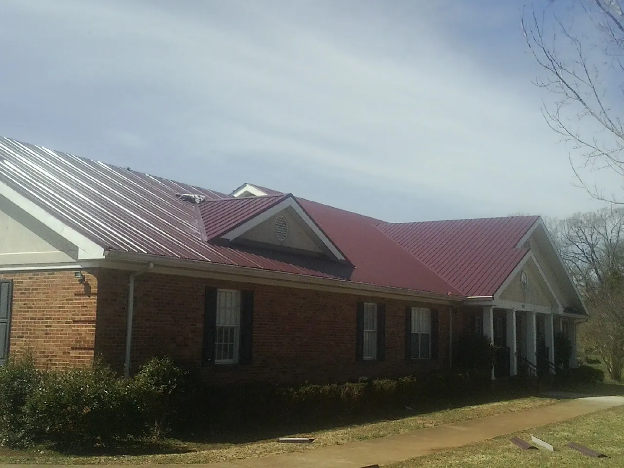 Red metal roof with gabled entries on a long brick building, from a Hail Damage Roof Repair job in Mapleton Depot